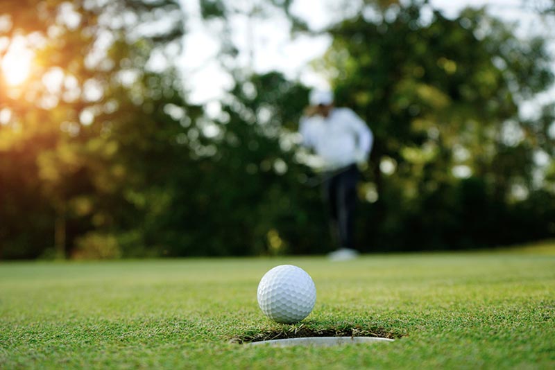 Golf ball about to roll in the hole with golfer in the background. 