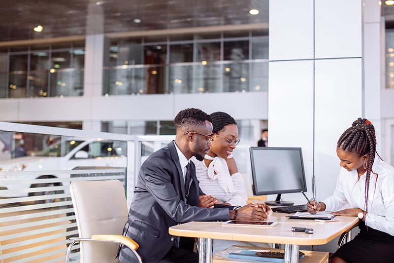 Couple at car dealership’s desk filling out payment paperwork. 