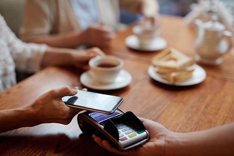 Customer paying for meal at the table using digital wallet on phone through a wireless terminal. 