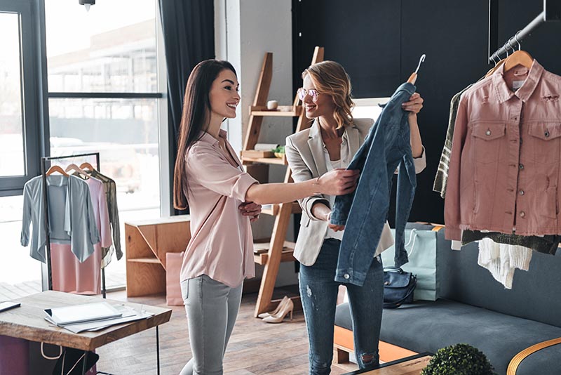 Retail employee showing customer denim jacket. 