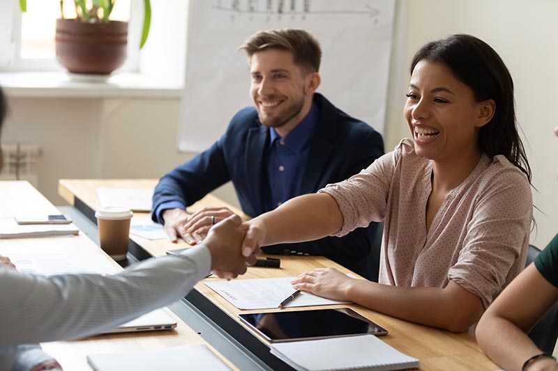 Woman shaking hands for partnerships with man in background.