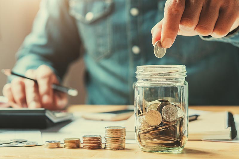 Businessman counting coins in a jar with calculator. 