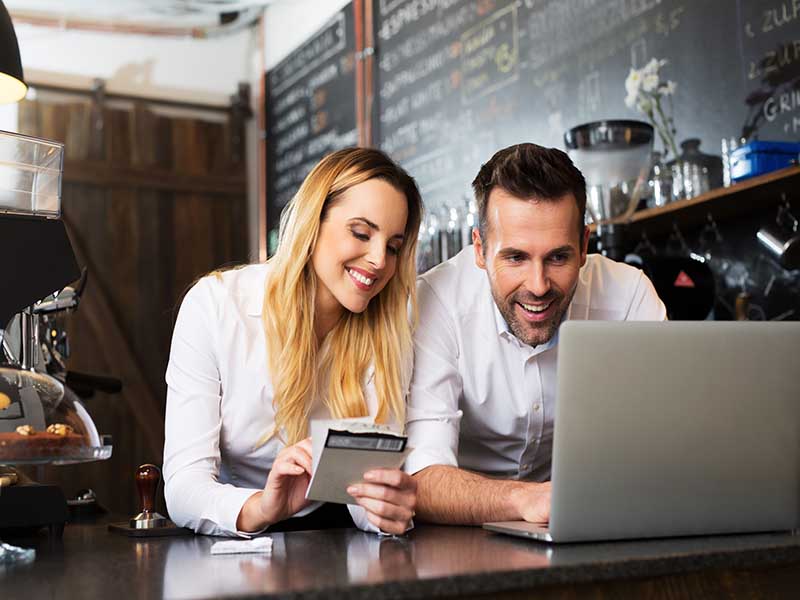 Business owners checking laptop behind counter at cafe. 